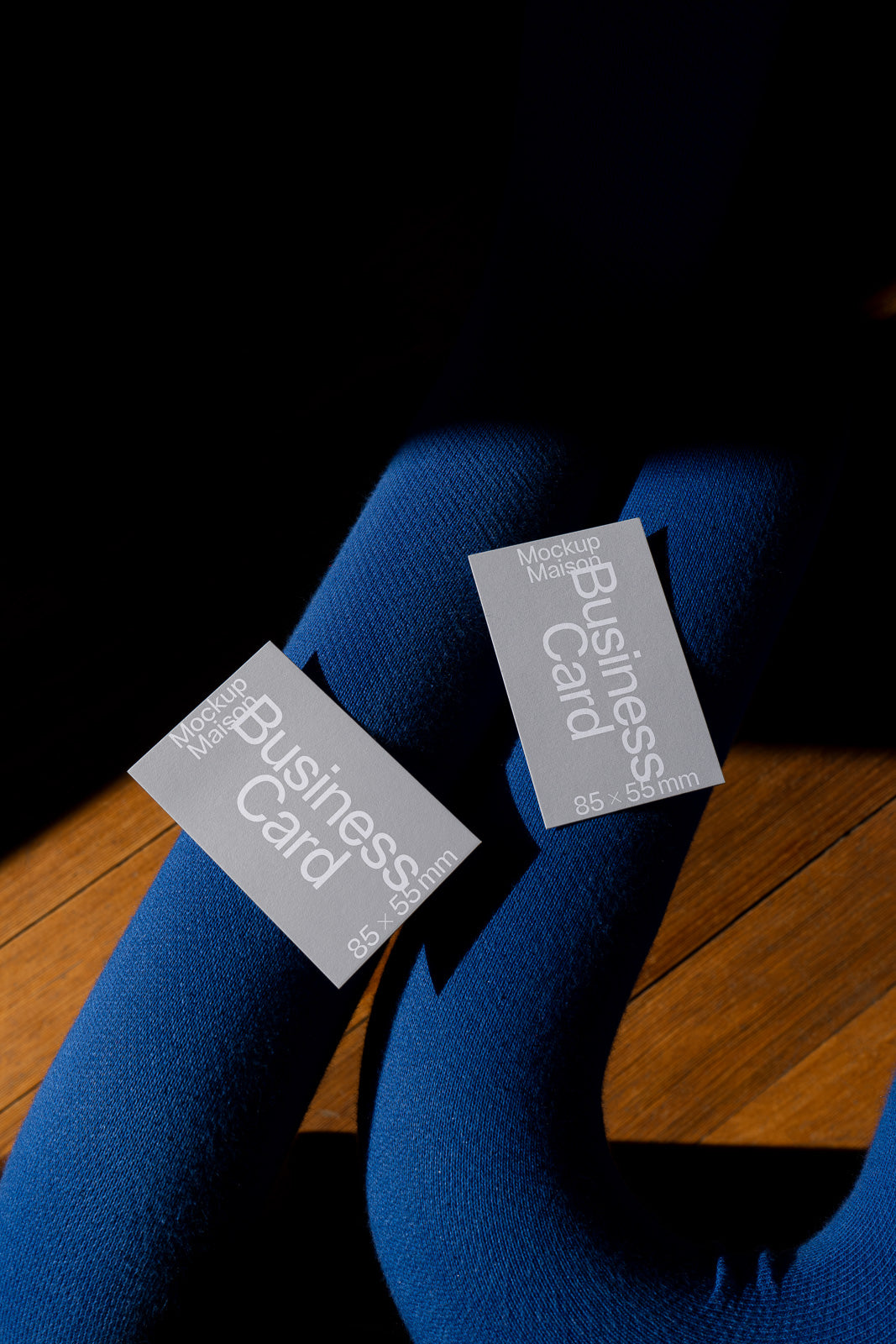 PSD mockup of two business cards displayed on a blue fabric surface, with shadows and wooden flooring in the background, highlighting card dimensions of 85x55mm.