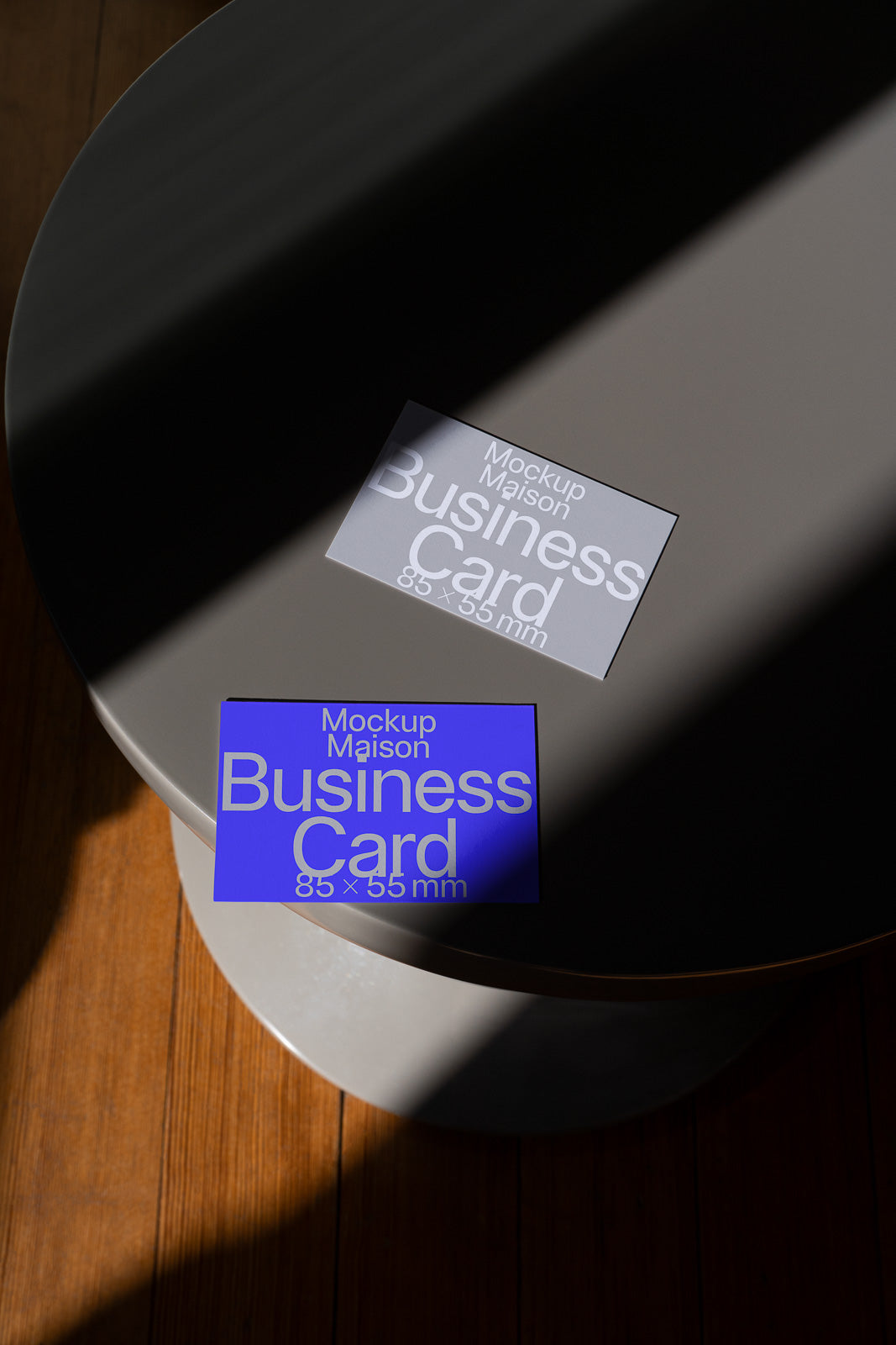 PSD mockup of two business cards on a round table with a shadow cast across, one card is blue and the other is gray, both displaying "Mockup Maison."