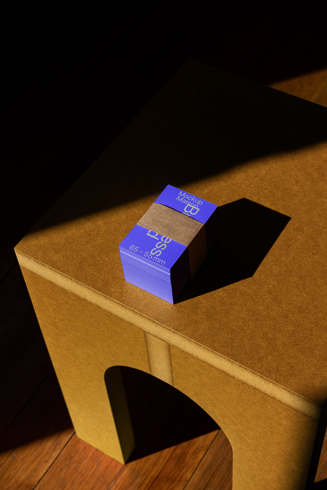 PSD mockup of a stack of blue business cards with dimensions 85x55mm, bound by a brown band, placed on a brown table with soft shadows.