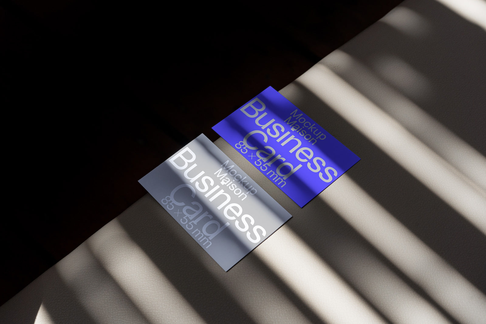 PSD mockup of two business cards, one gray and one blue, placed on a surface with striped light shadows.