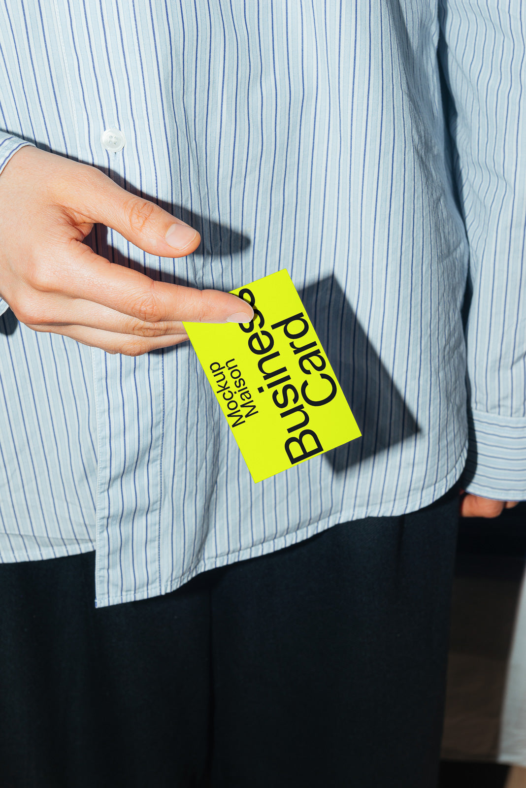 PSD mockup of a person holding a neon yellow business card with bold black text, against a striped shirt background.