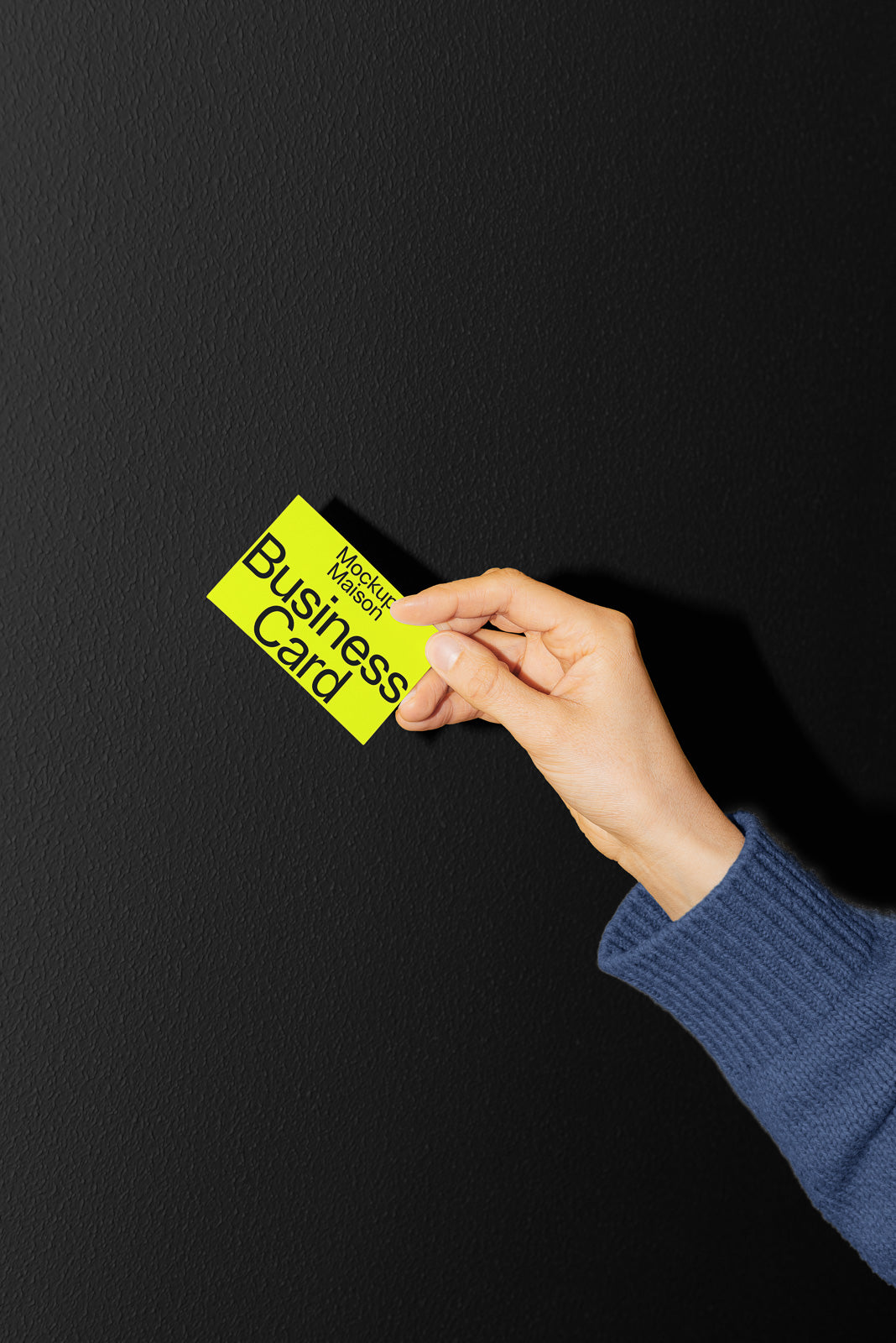 PSD mockup of a hand holding a yellow business card against a dark textured background.
