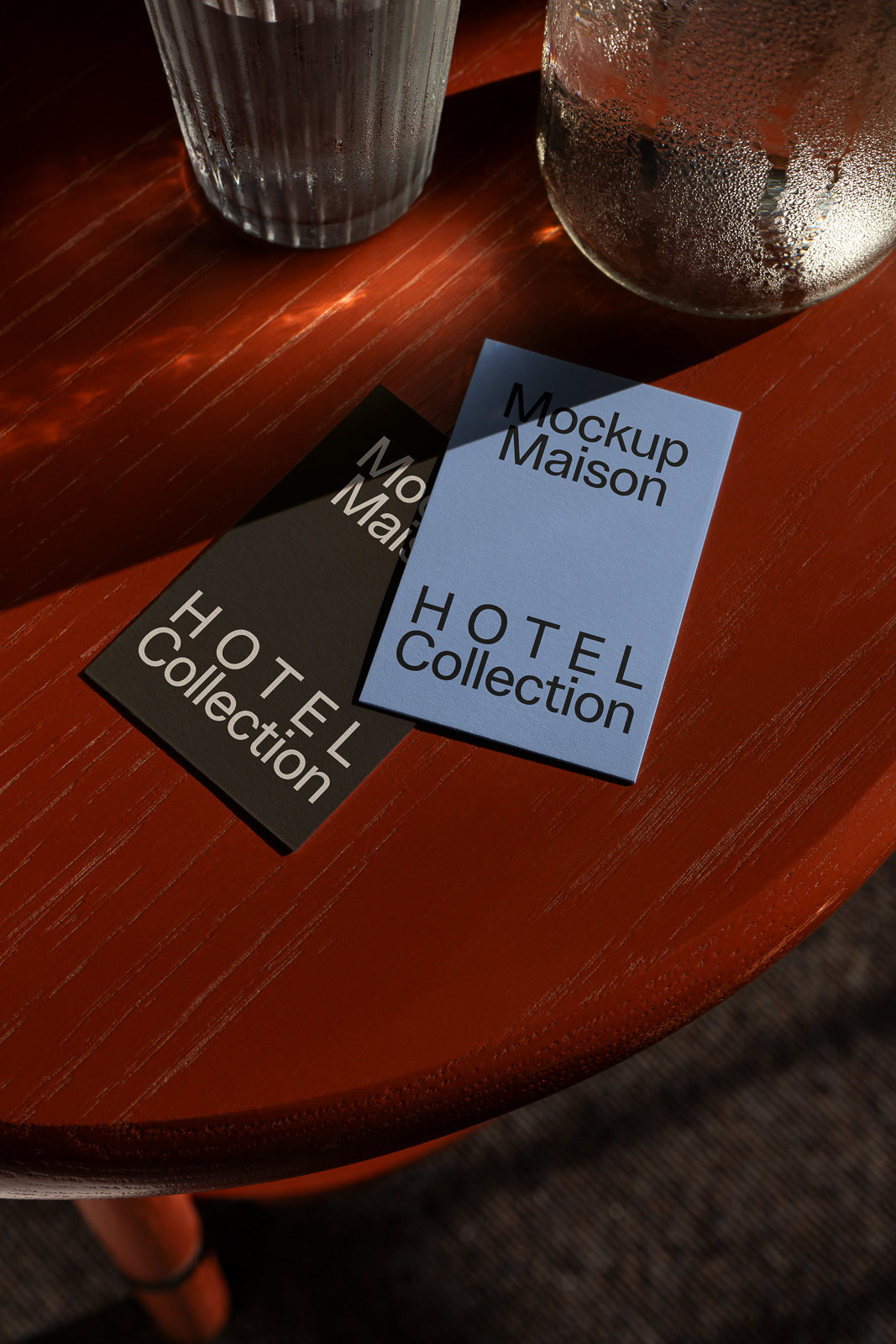 PSD mockup of two cards labeled "Hotel Collection" placed on a wooden table, beside a glass and a cup, under natural light.