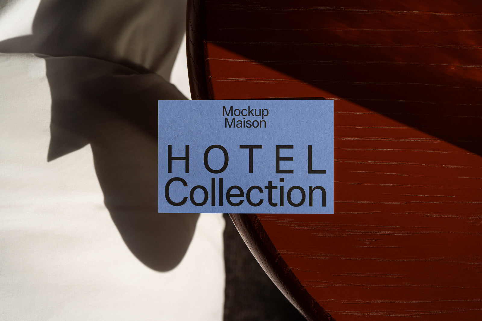 PSD mockup of a blue card titled "Mockup Maison HOTEL Collection" set on a wooden surface with soft shadows and light.