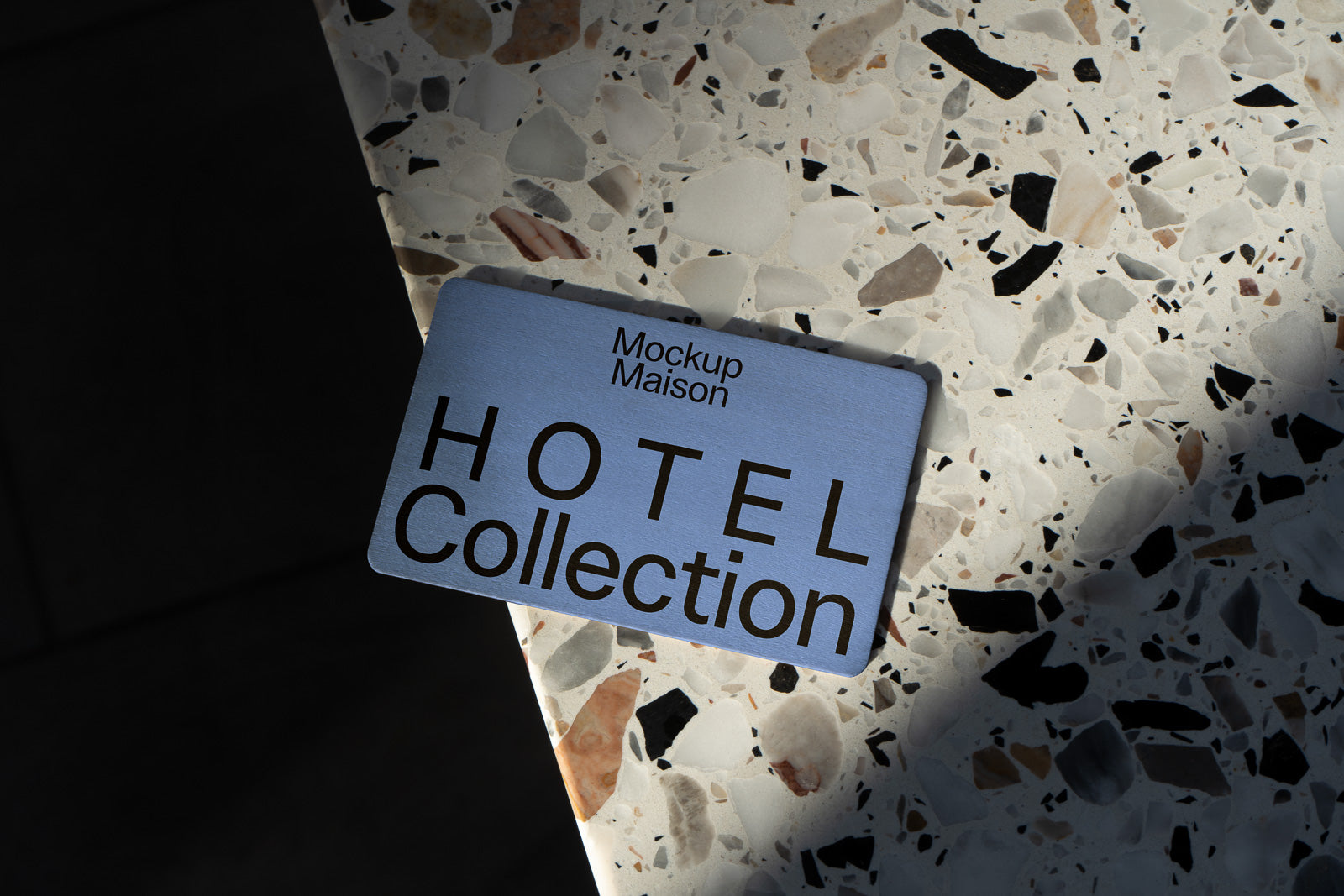 PSD mockup of a card displaying "Hotel Collection" laying on a terrazzo surface with varied textures and colors, partially in shadow.