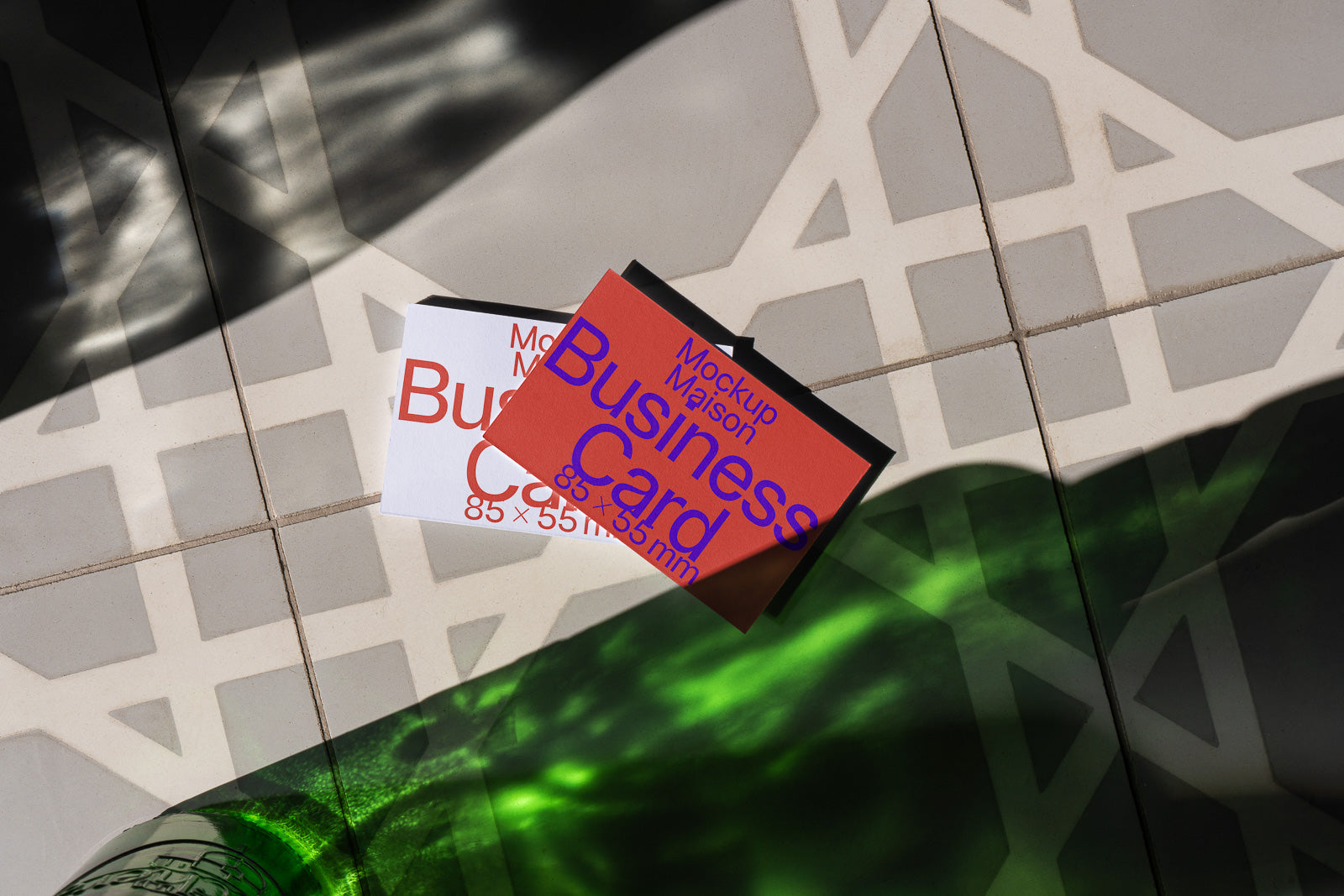 PSD mockup of two business cards on a patterned tile surface with shadows and green light reflections.