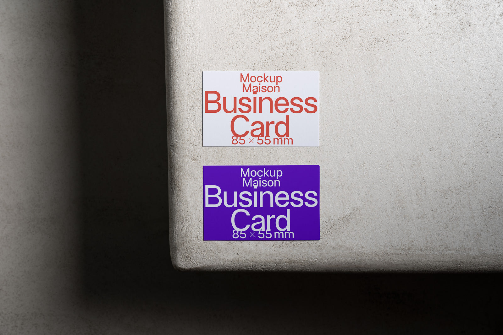 PSD mockup of two business cards, one red-tinted on white and one white on purple, both sized 85 x 55 mm, displayed on a textured surface corner.