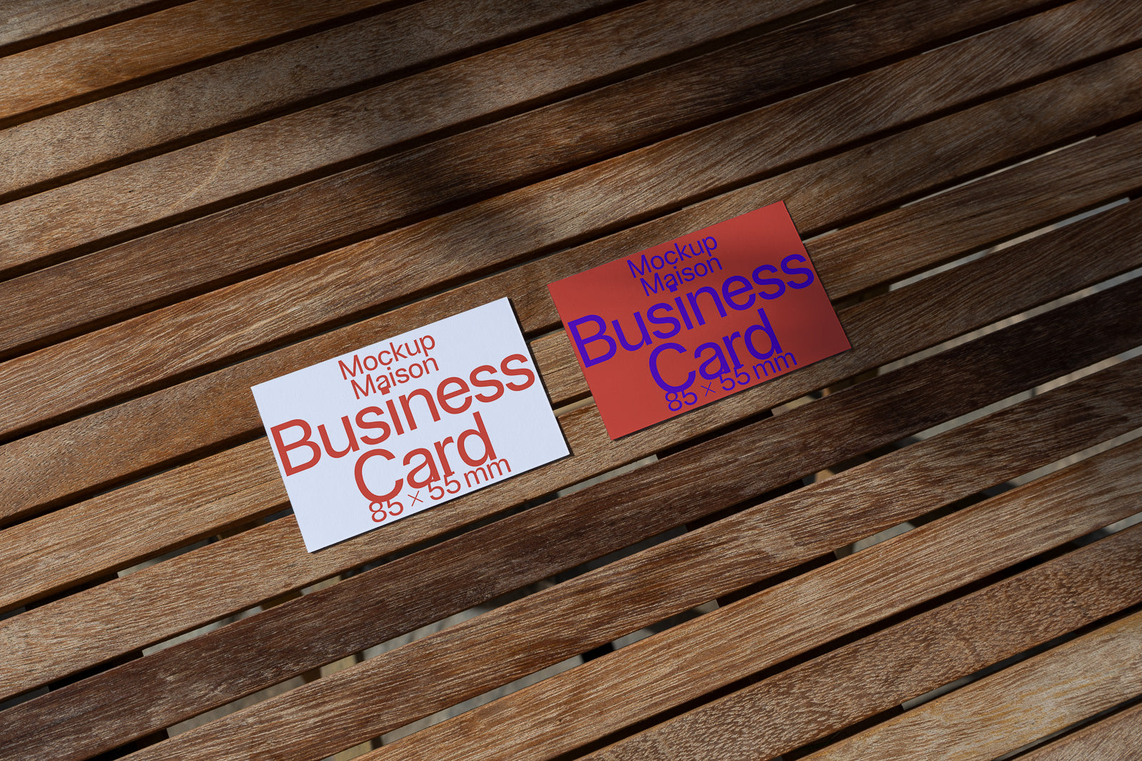 PSD mockup of two business cards, one white and one red, placed on a wooden surface. Both display the dimensions 85 x 55 mm with bold typography.