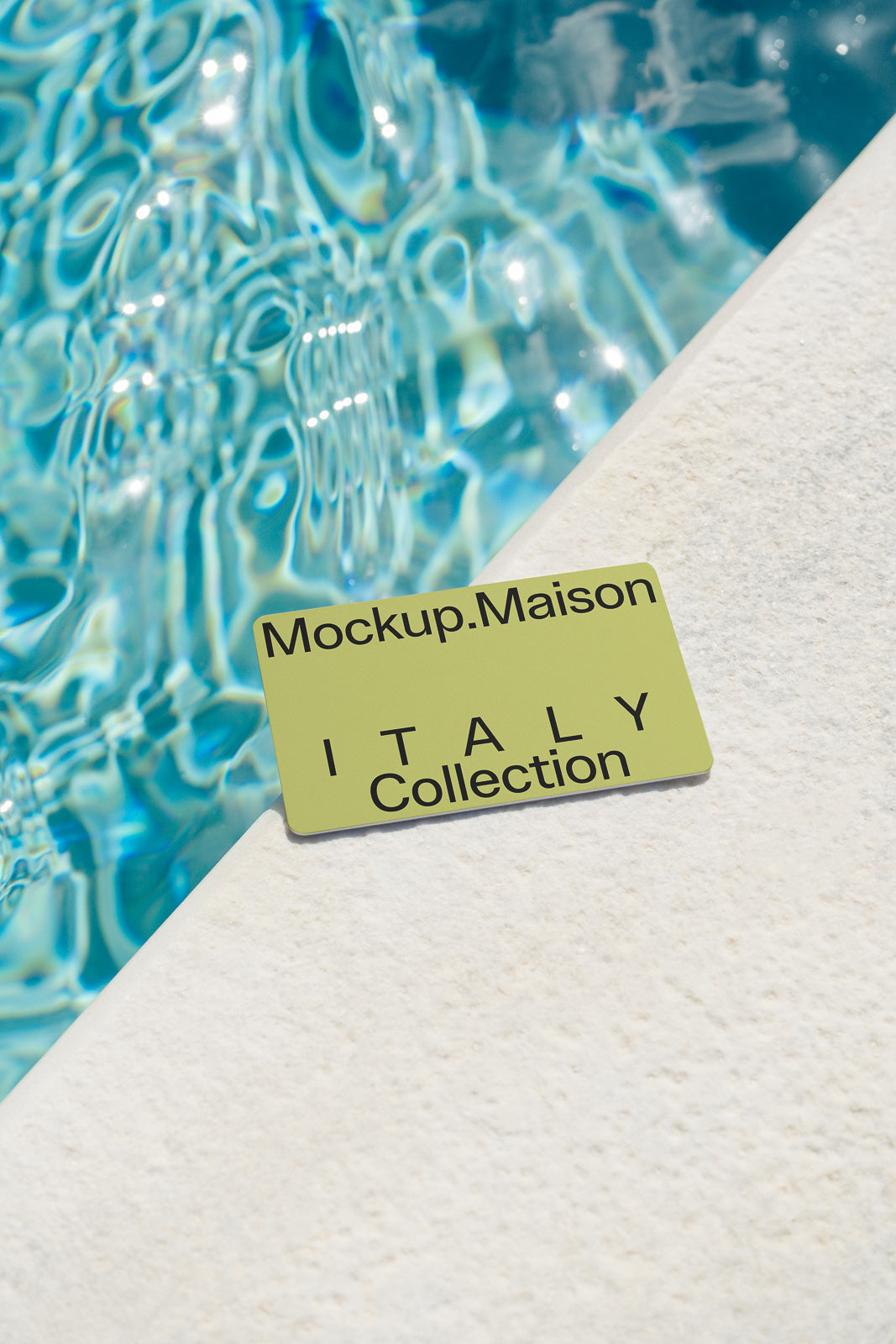PSD mockup of a rectangular card on a stone surface beside a pool, displaying the text "Mockup.Maison ITALY Collection" with sunlight reflections.