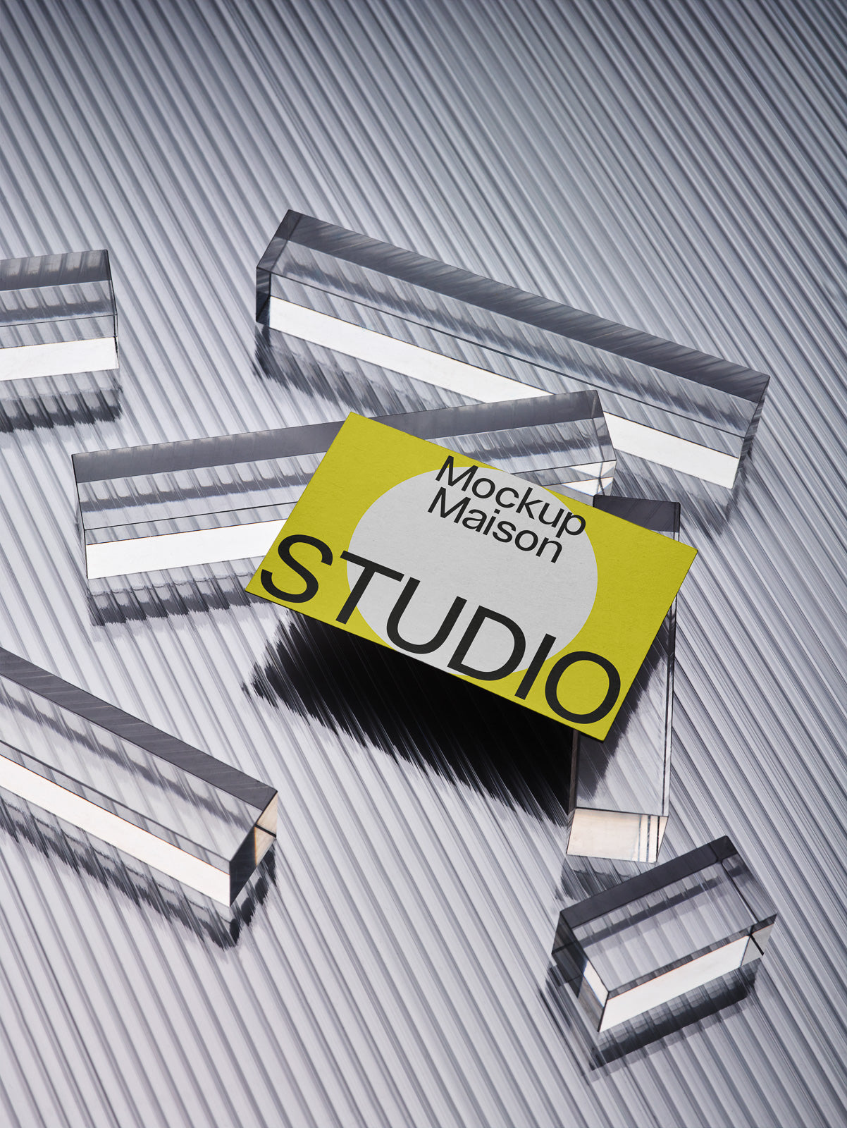 PSD mockup of a business card on a corrugated metallic surface surrounded by transparent acrylic prisms, casting reflections and shadows.