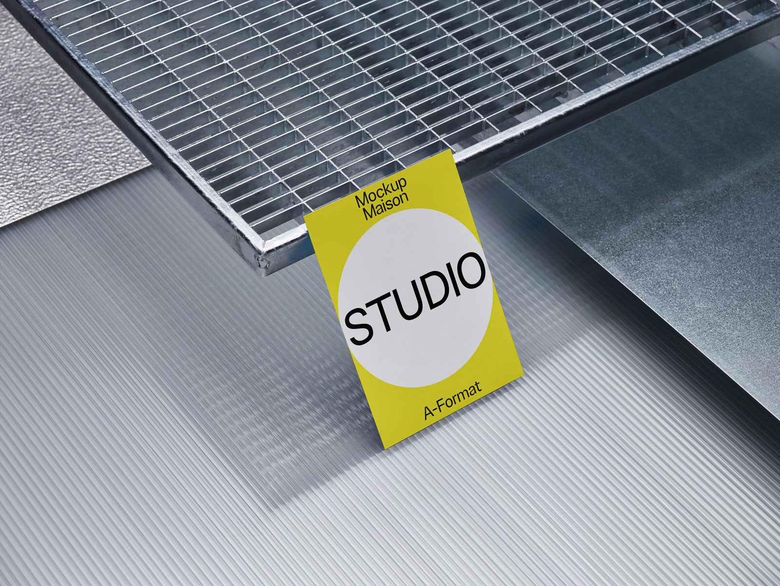 PSD mockup of a yellow card labeled "STUDIO" positioned under a metallic grid and resting on textured surfaces.