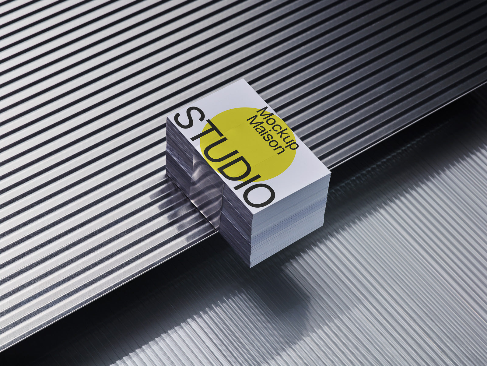 PSD mockup of a stack of business cards with "Mockup Maison Studio" on a textured metallic surface, reflecting light and casting shadows.