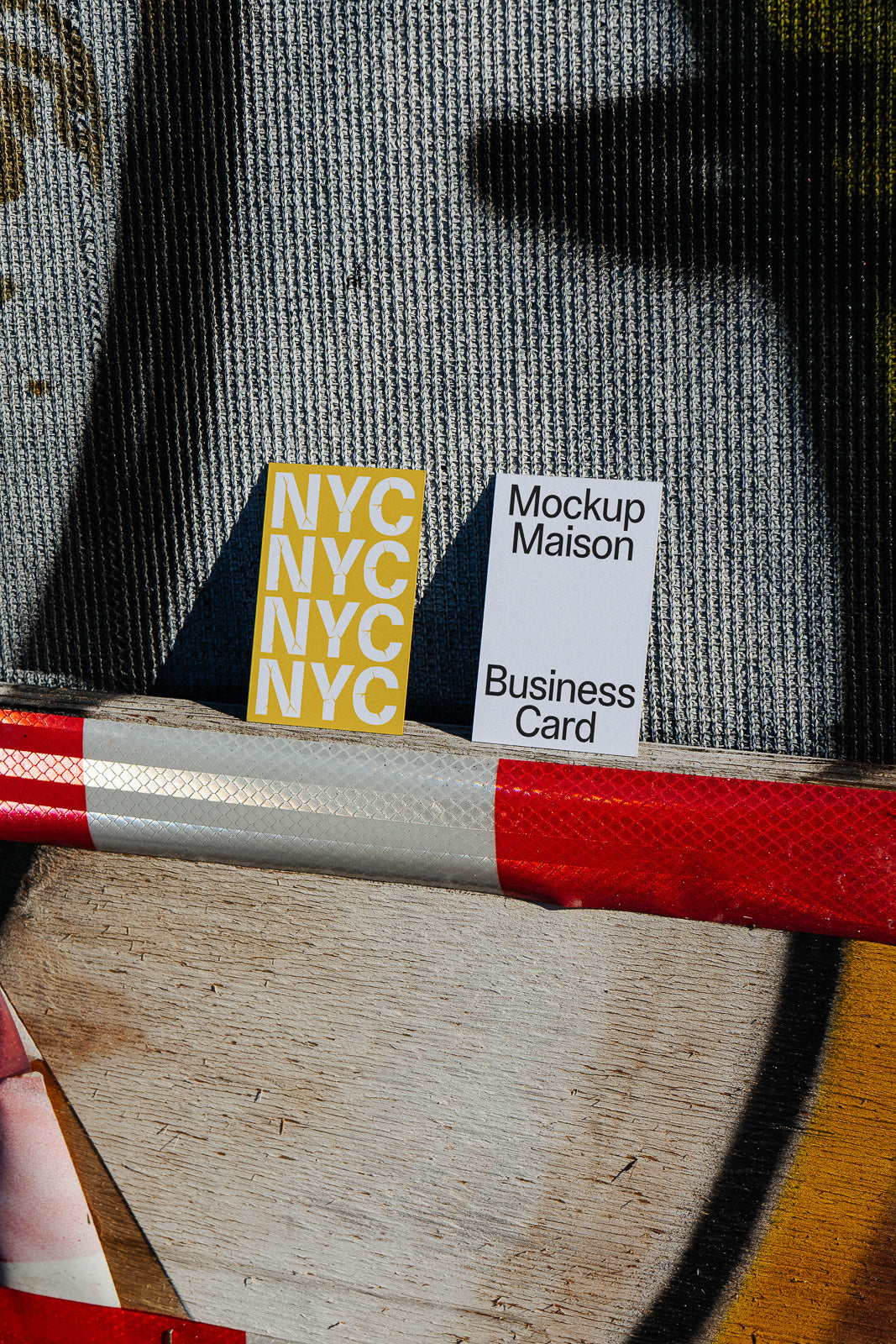 PSD mockup of two business cards leaning against a textured surface, one card with NYC letters in bold on yellow, the other labeled Mockup Maison.