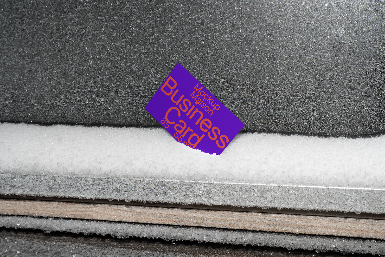 PSD mockup of a business card partially buried in snow against a textured, dark background, emphasizing cold and contrast in the design.