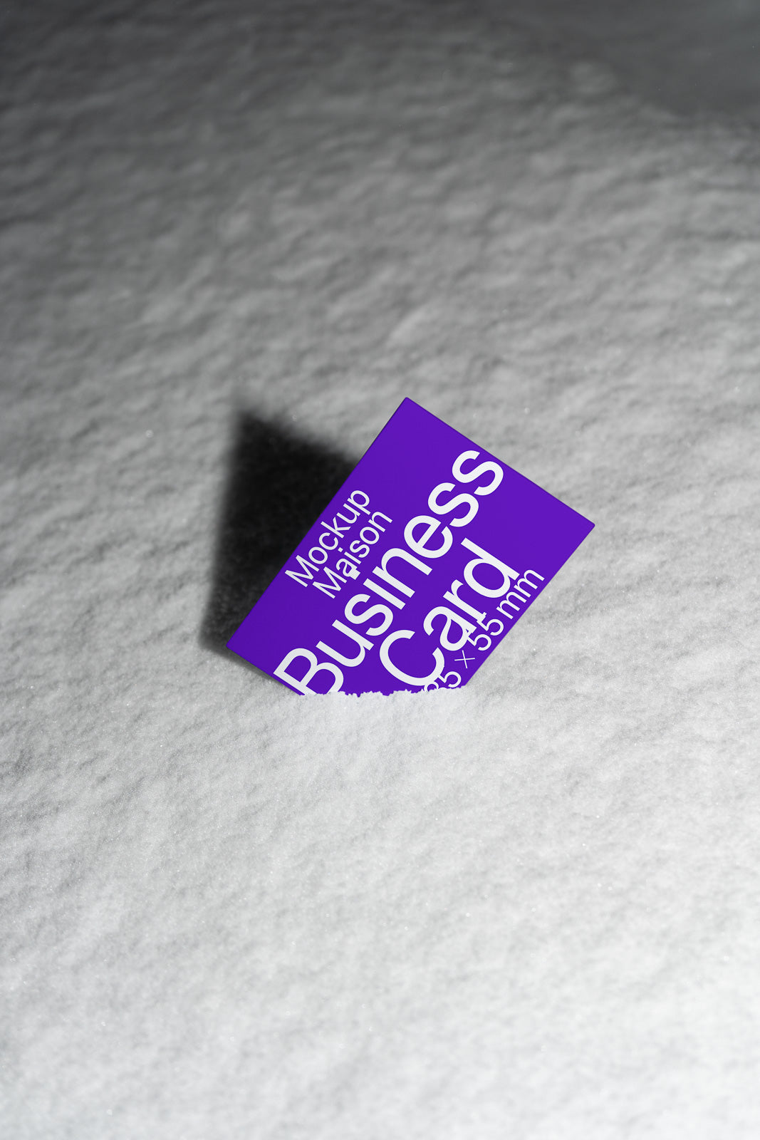 PSD mockup of a purple business card partially embedded in a textured snowy surface, casting a distinct shadow to the left.