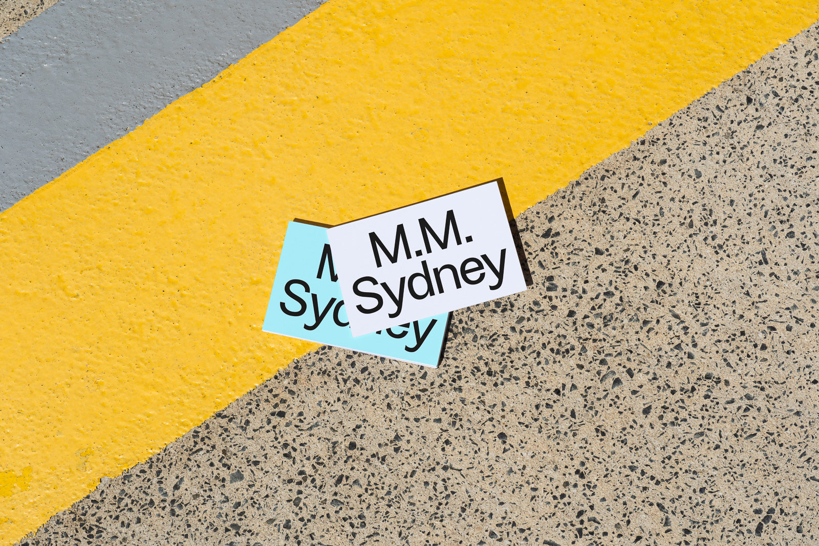 PSD mockup of two overlapping business cards on a textured surface with a yellow stripe, displaying "M.M. Sydney" text.