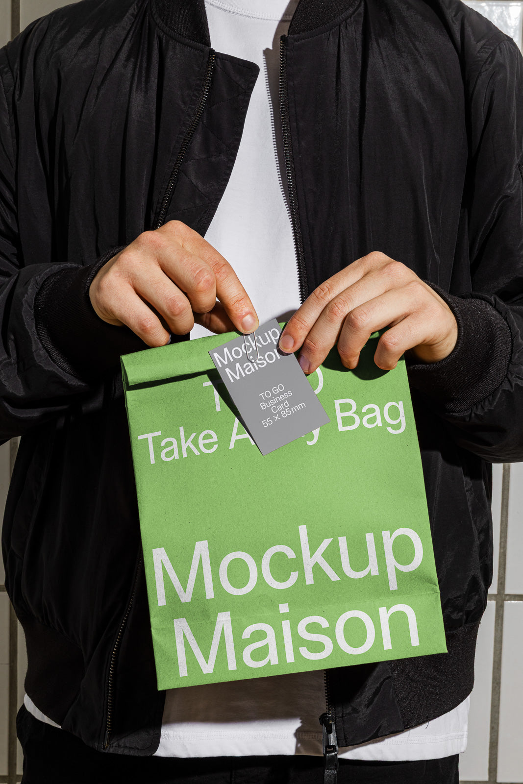 PSD mockup of a person holding a green paper bag labeled "Mockup Maison" with a small tag.