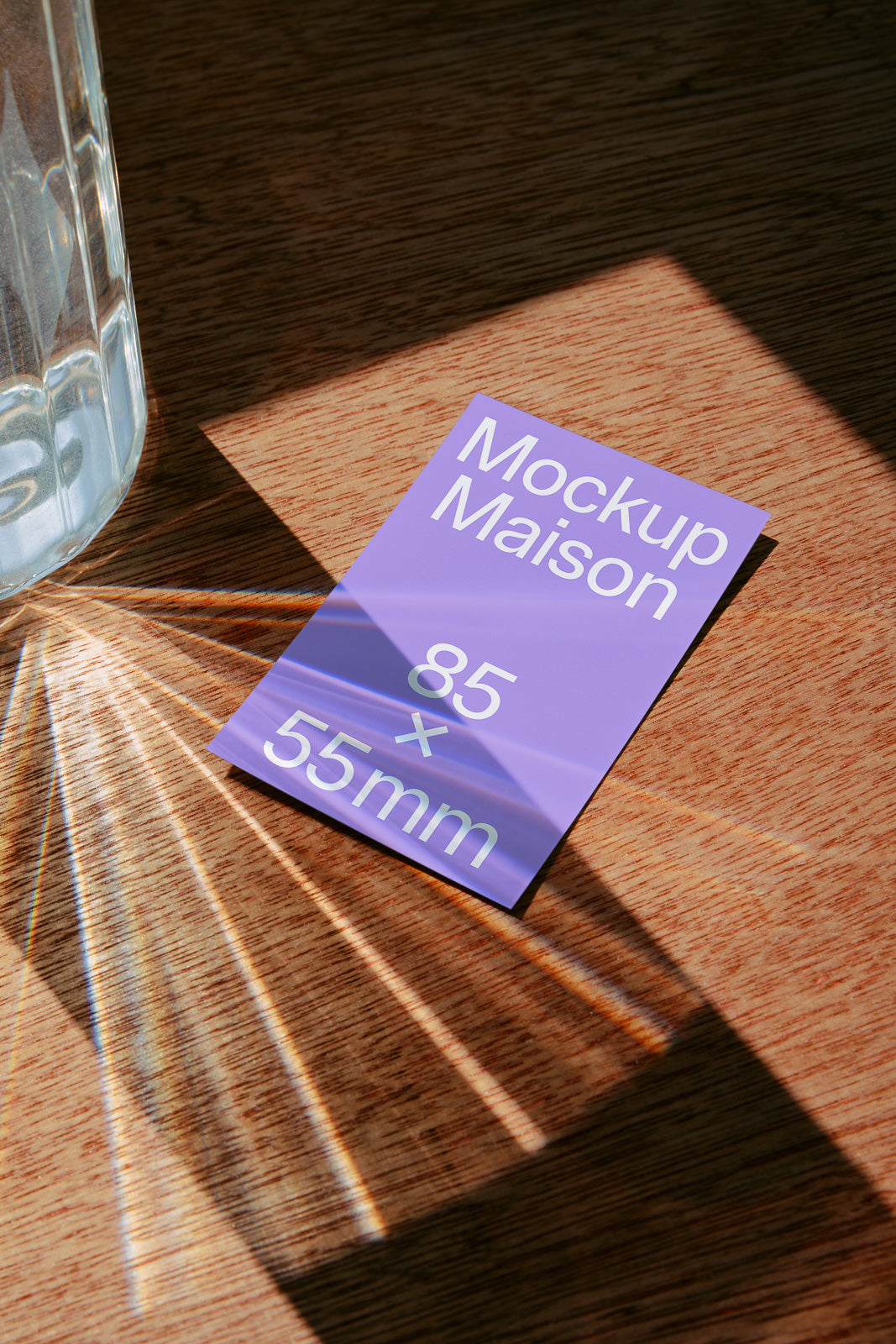 PSD mockup of a purple 85x55mm card on a wooden surface, with light reflections casting patterns from a nearby glass.