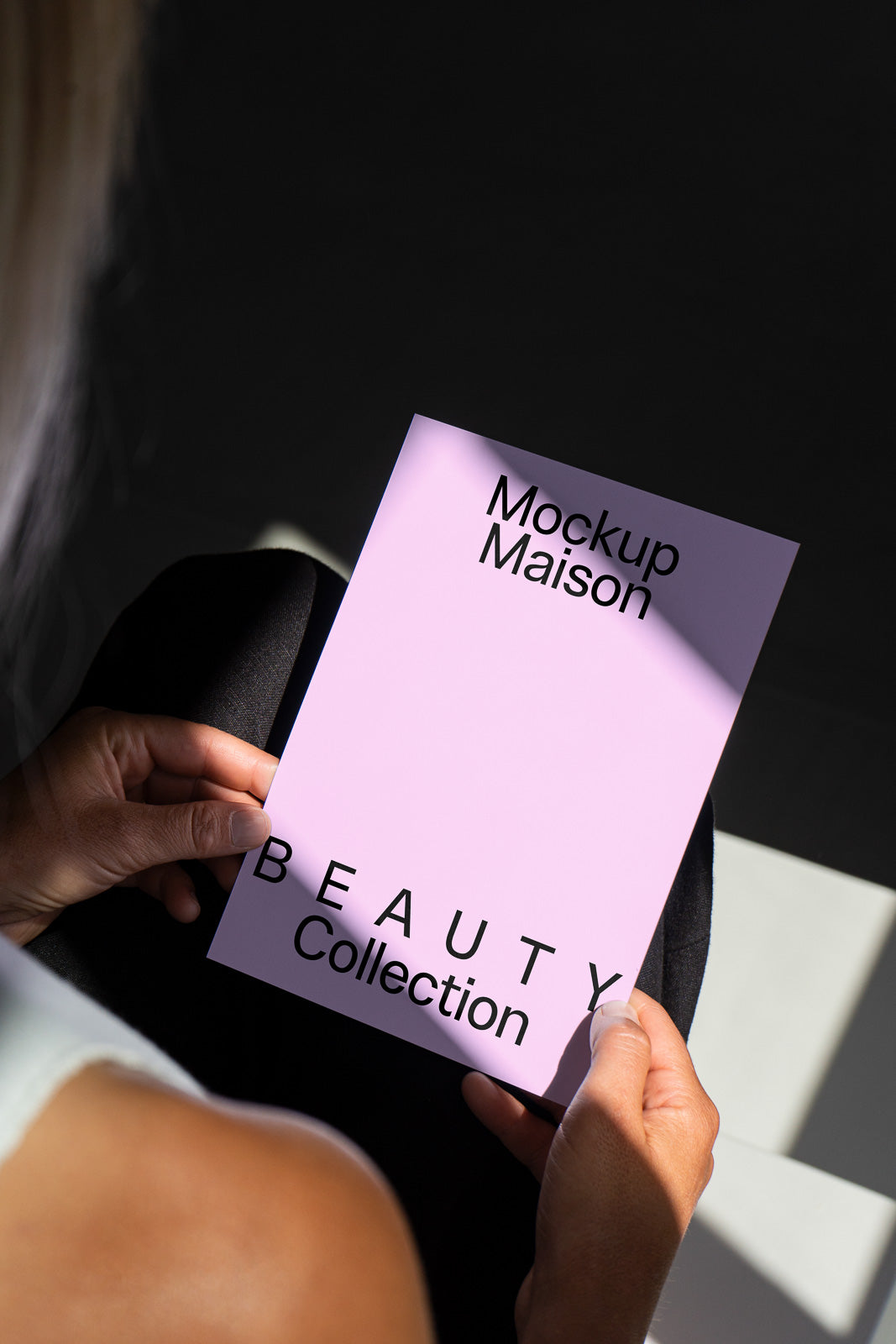 PSD mockup of a person holding a pink card labeled "Mockup Maison Beauty Collection" in black text, illuminated by soft lighting.