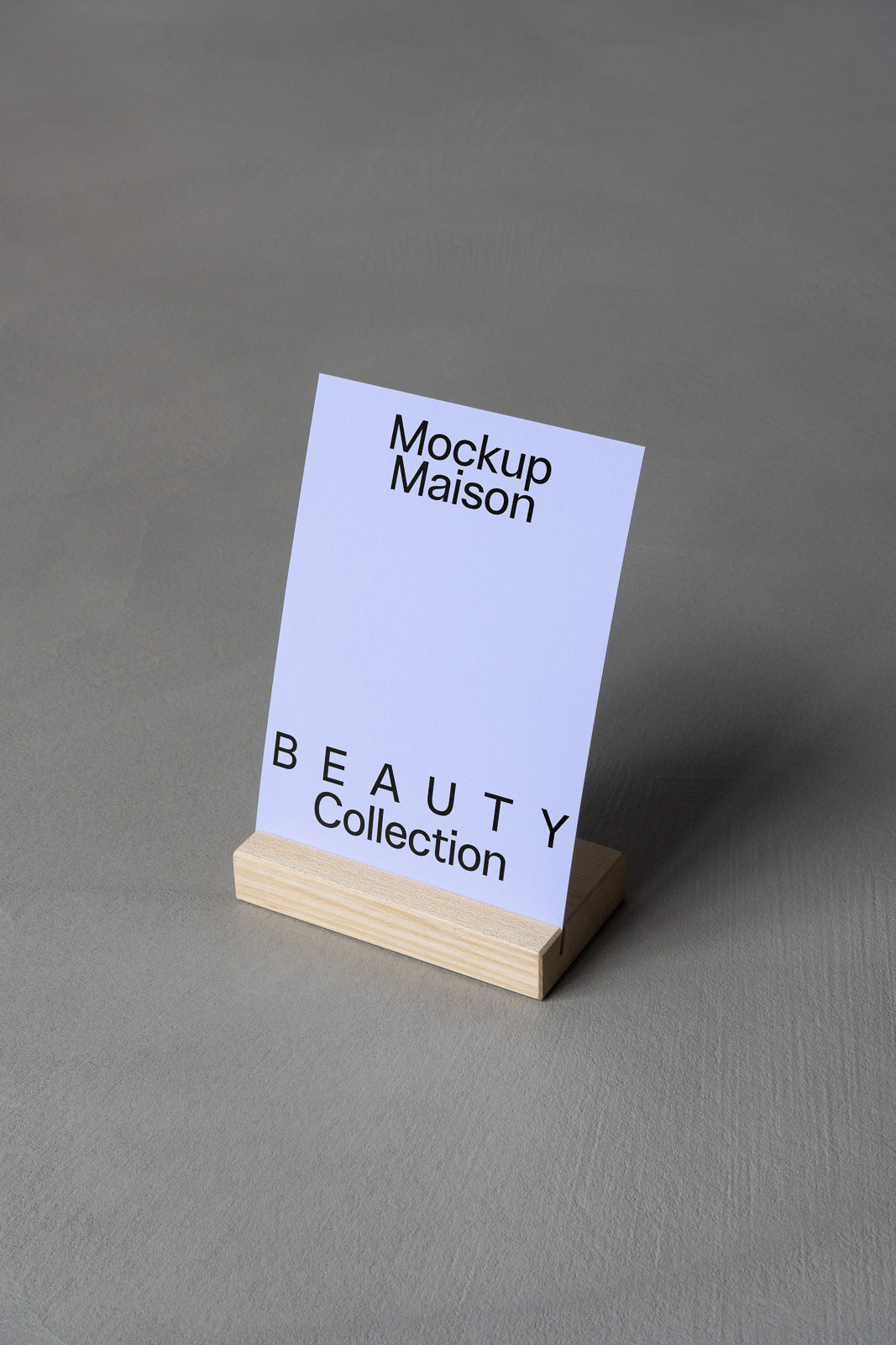 PSD mockup of a minimalist card displaying "Mockup Maison" and "BEAUTY Collection" on a wooden stand against a gray background.
