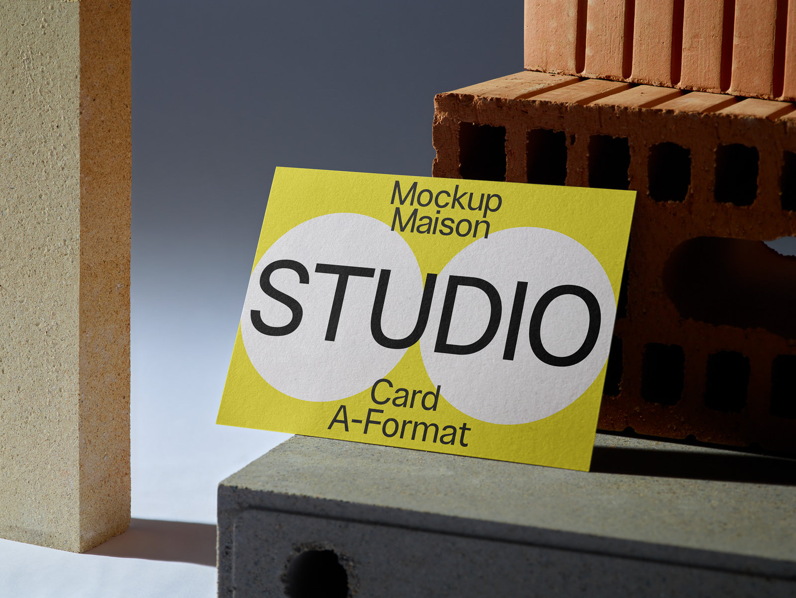 PSD mockup of a yellow card titled "STUDIO" resting against bricks and concrete blocks, showcasing bold black text on a clean, geometric design.