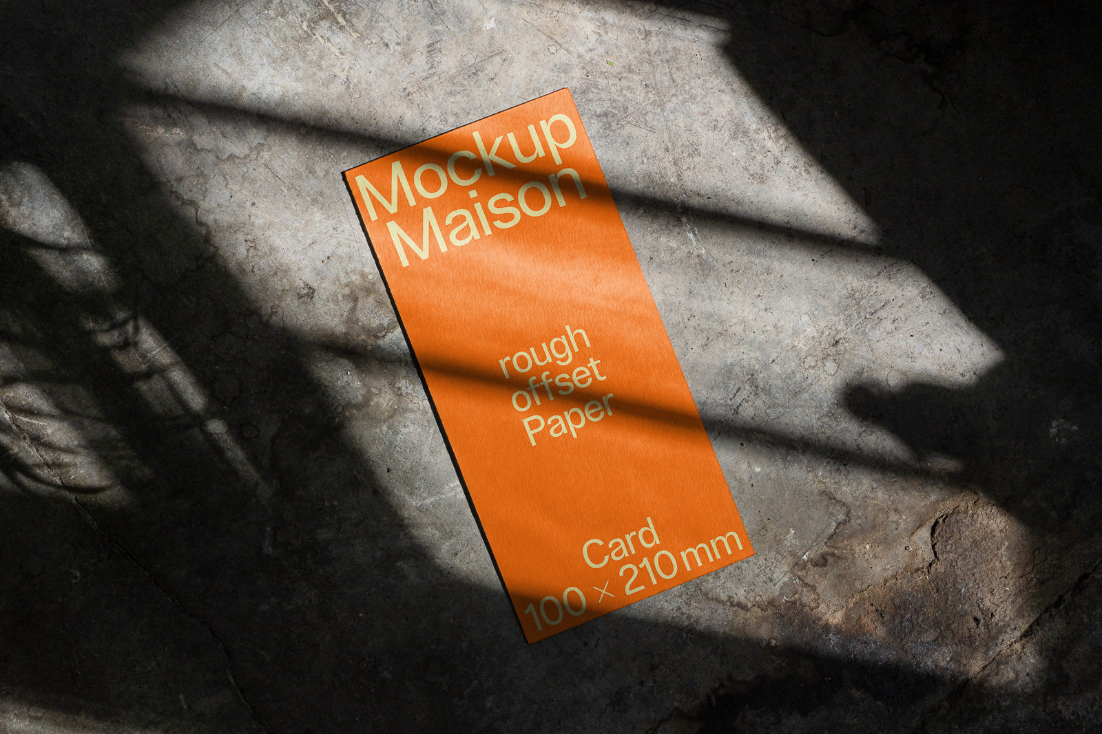 PSD mockup of an orange card displaying "Mockup Maison" and "rough offset paper" against a textured stone surface, partially shadowed.
