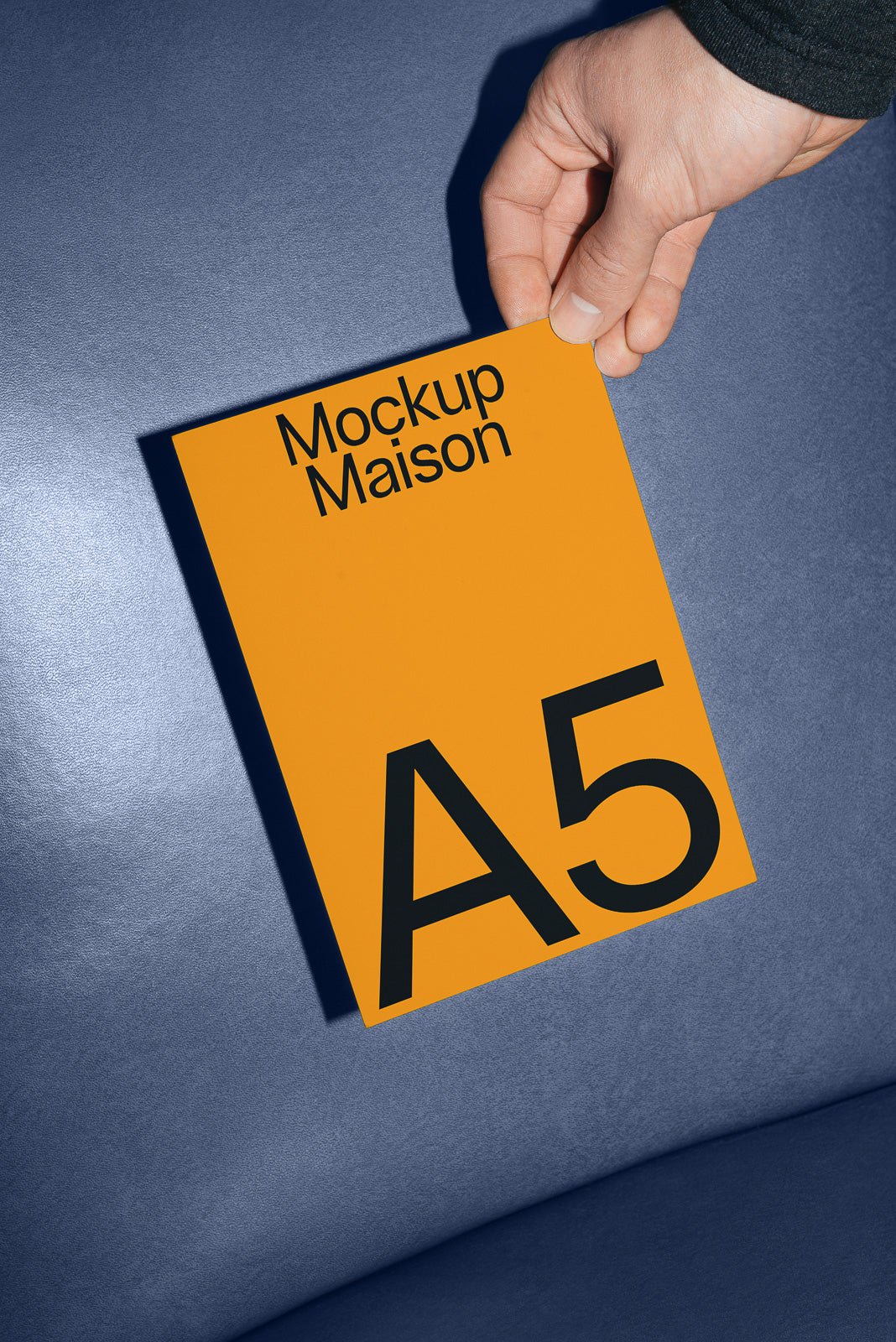PSD mockup of a hand holding an orange A5 card labeled "Mockup Maison" against a blue background.