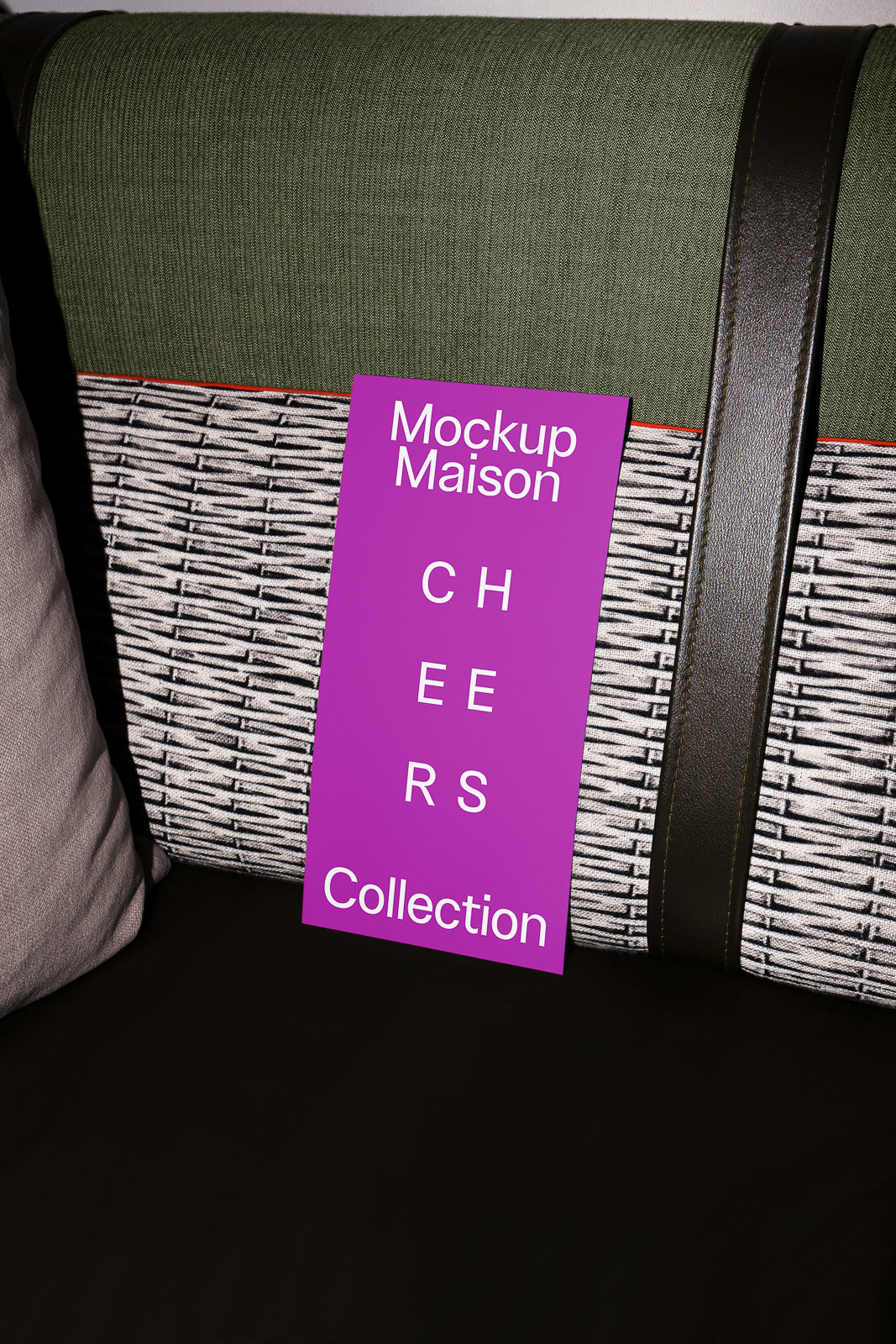 PSD mockup of a purple card with "Mockup Maison Cheers Collection" text, leaning against a textured cushion with green, black, and beige tones.