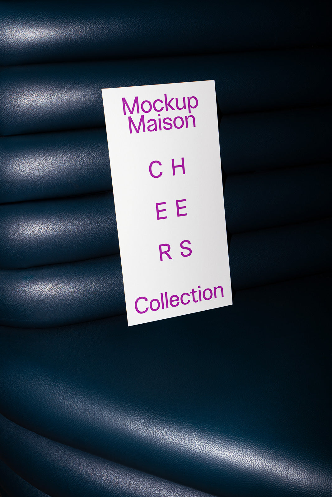PSD mockup of a rectangular card placed against blue leather seating with text reading "Mockup Maison CHEERS Collection" in purple.