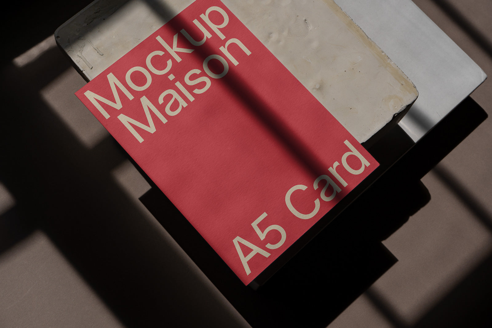 PSD mockup of a red A5 card with the text "Mockup Maison" slightly tilted against a textured surface, with shadows cast diagonally across the scene.