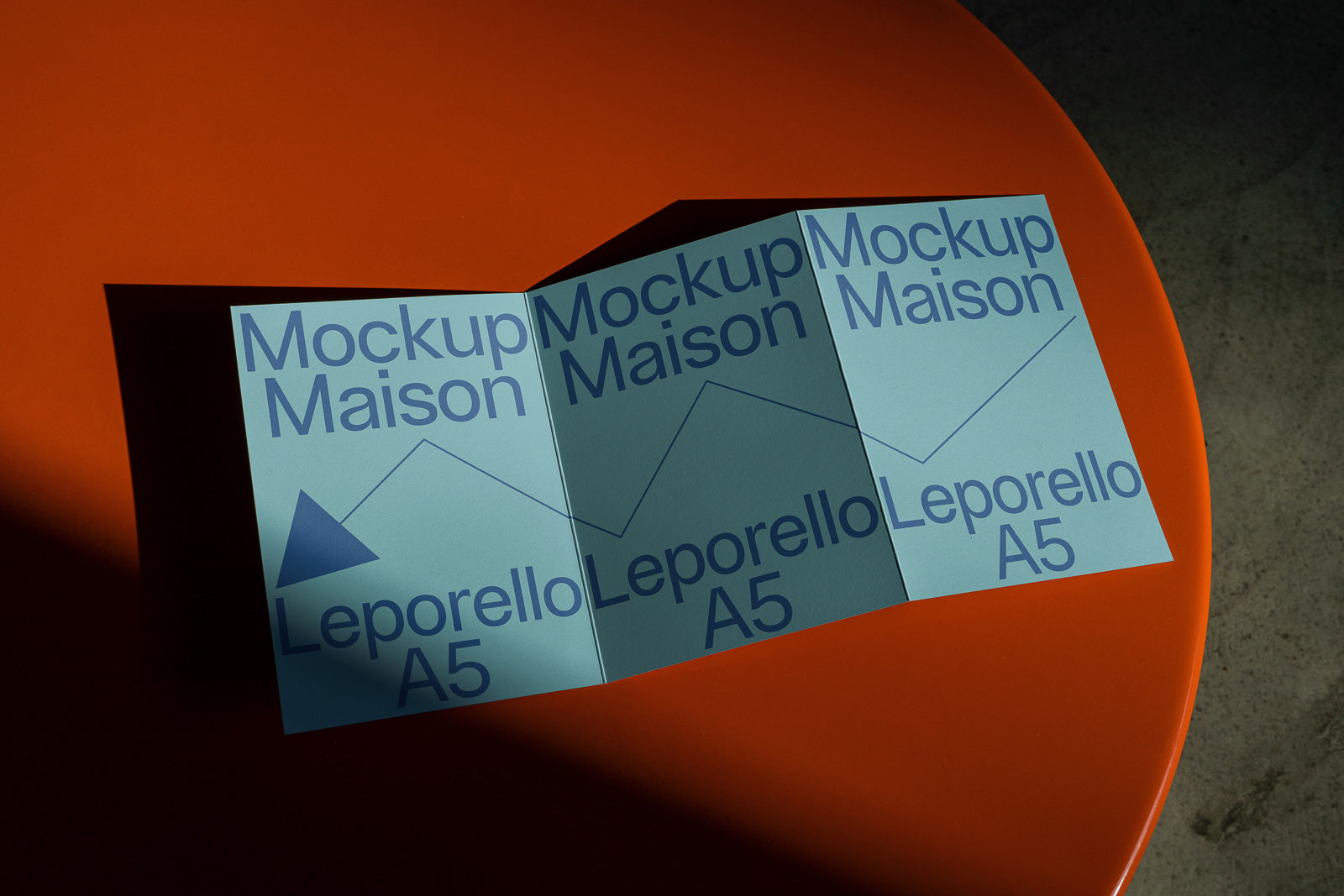 PSD mockup of a folded Leporello A5 brochure with blue text, titled "Mockup Maison," displayed on an orange surface with elongated shadows.