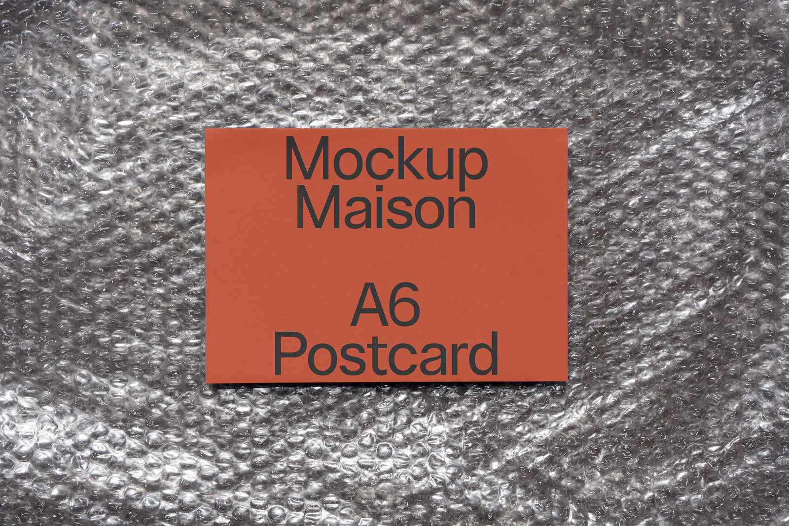 PSD mockup of an A6 postcard with "Mockup Maison" text on a red background, placed on a textured silver surface.