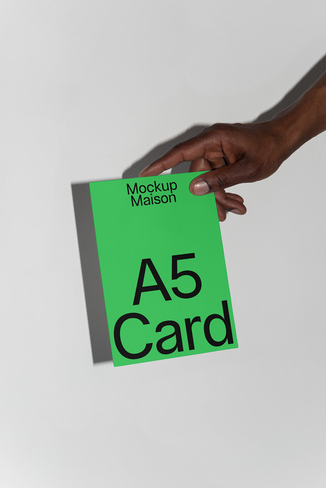 PSD mockup of a hand holding a bright green A5 card with "Mockup Maison" text on top against a gray background.