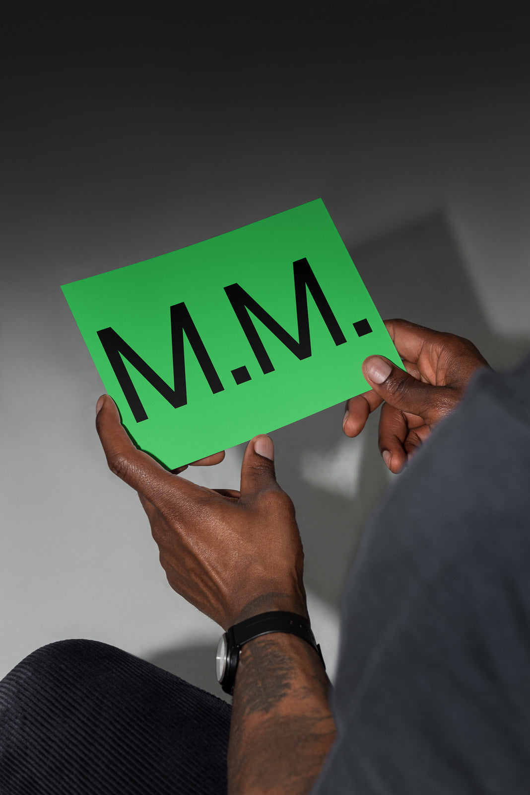 PSD mockup of a person holding a green card with "M.M." printed in large black letters.