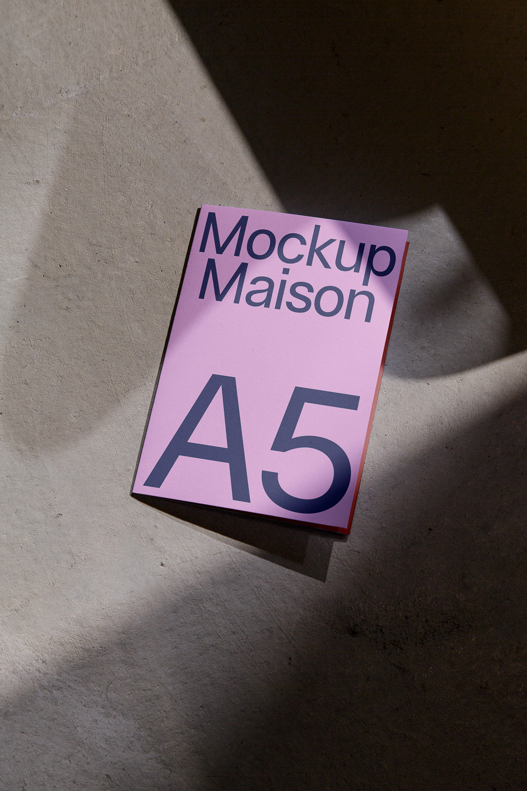 PSD mockup of an A5 booklet with "Mockup Maison" text on a pink cover, set against a textured gray surface with shadow play.
