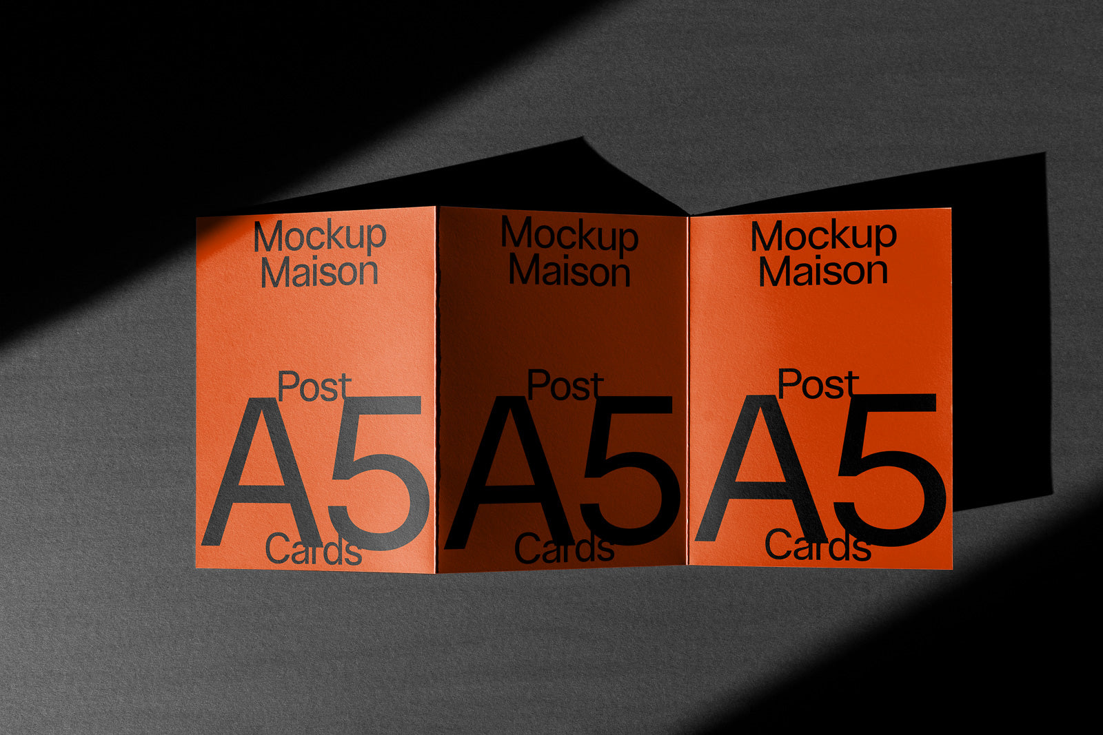 PSD mockup of three standing A5 cards with bold black text on an orange background, casting shadows on a dark surface.