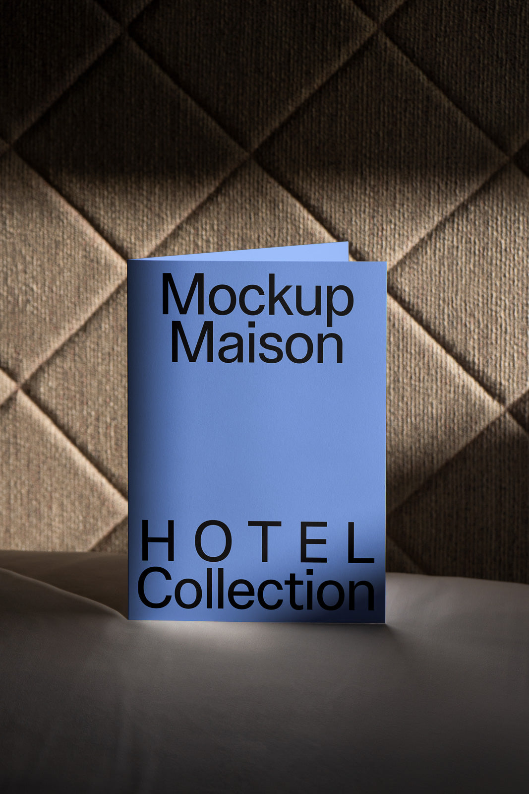 PSD mockup of a blue booklet with "Mockup Maison HOTEL Collection" text, standing against a decorative quilted background.