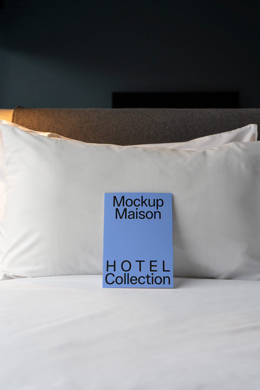 PSD mockup of a blue card with "Mockup Maison" and "Hotel Collection" text, standing against white pillows on a bed.