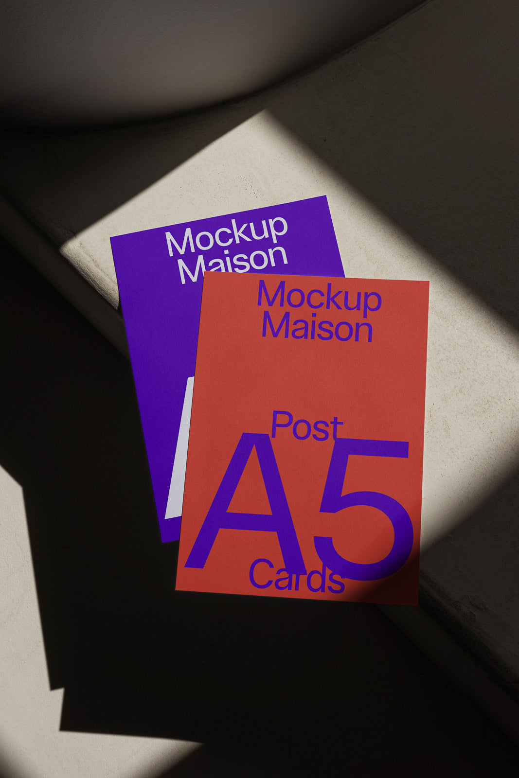 PSD mockup of two A5 postcards, one red and one purple, arranged on a sunlit surface, with bold text reading "Mockup Maison" and "Post A5 Cards".