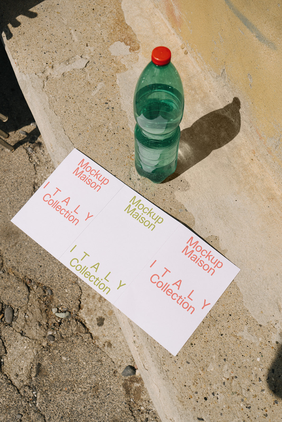 PSD mockup of a green plastic bottle with red cap next to two sheets labeled "Mockup Maison Italy Collection" placed on a stone surface.