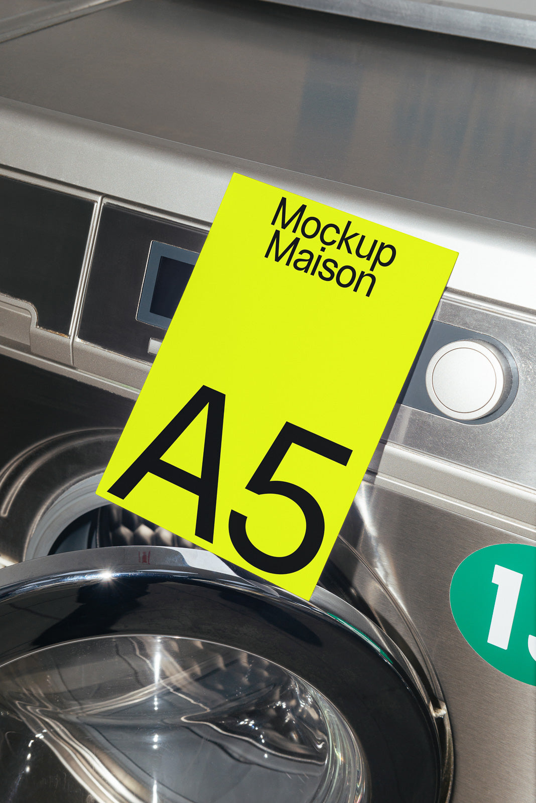 PSD mockup of an A5 paper with "Mockup Maison" text leaning against a metallic surface near a washing machine door.