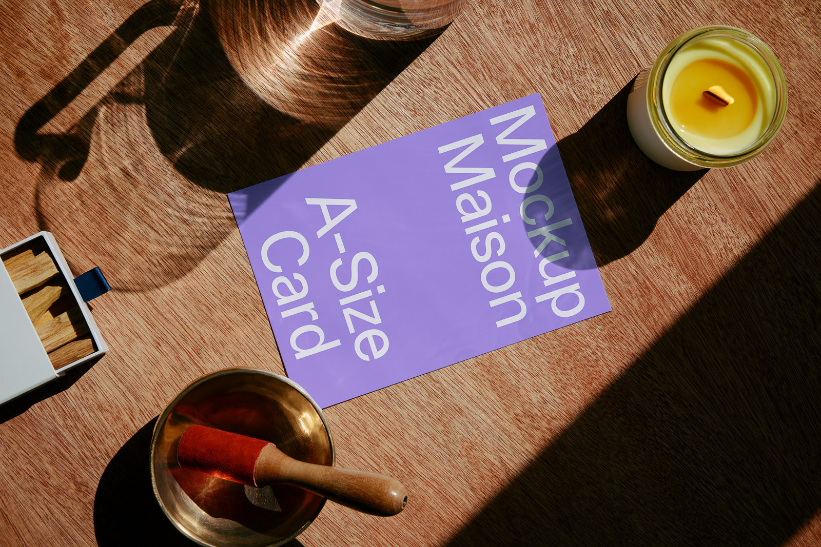 PSD mockup of A-size card on wooden surface with a candle, matches, and a singing bowl nearby, in warm natural light.