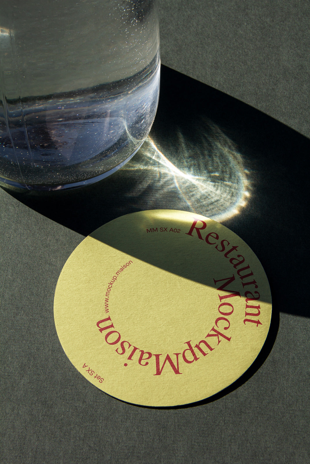 PSD mockup of a round restaurant coaster in earthy tones, placed partially under a glass container with light reflections creating textures on a dark background.