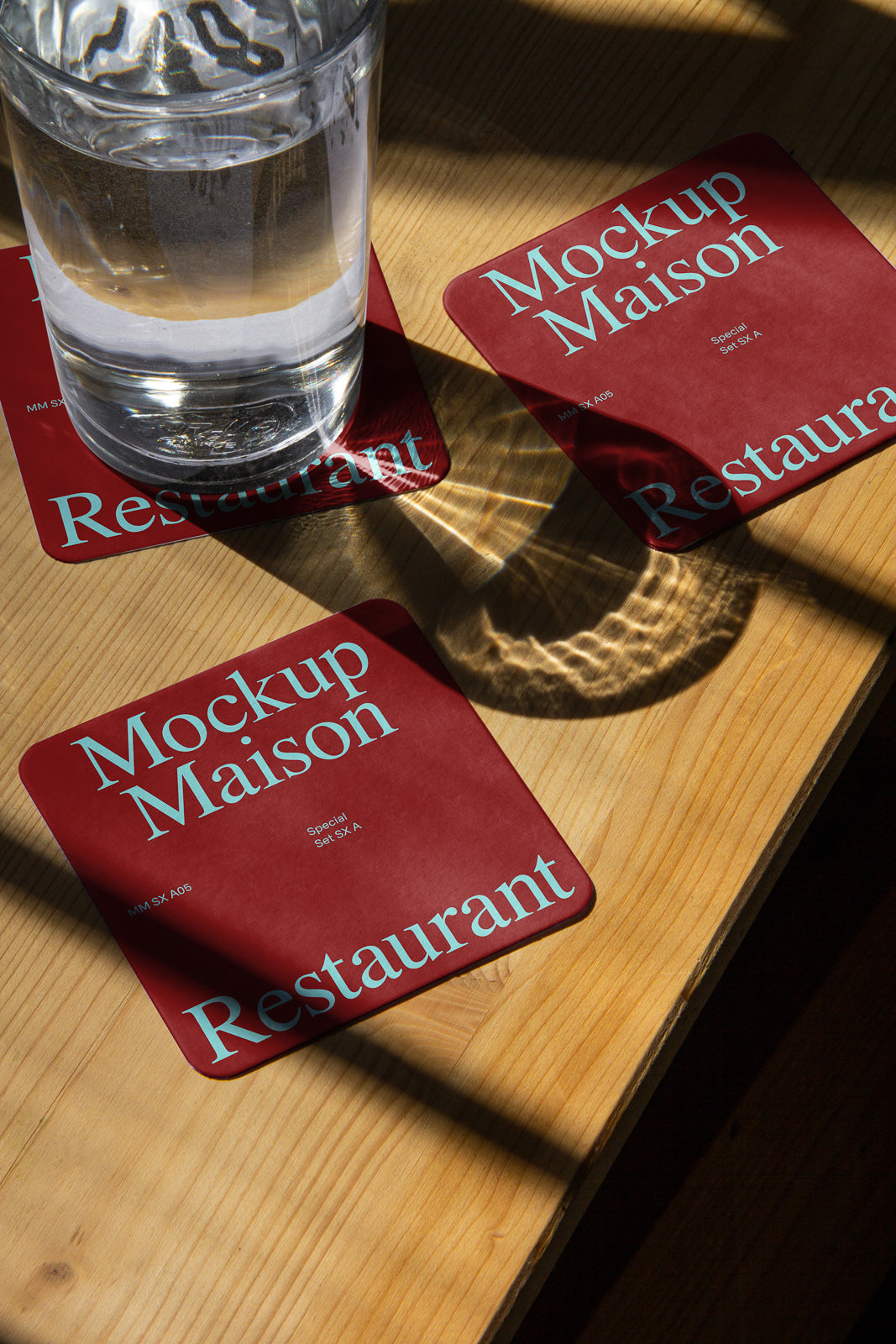 PSD mockup of three red restaurant coasters with the text "Mockup Maison" on a wooden table, with a glass of water casting shadows.