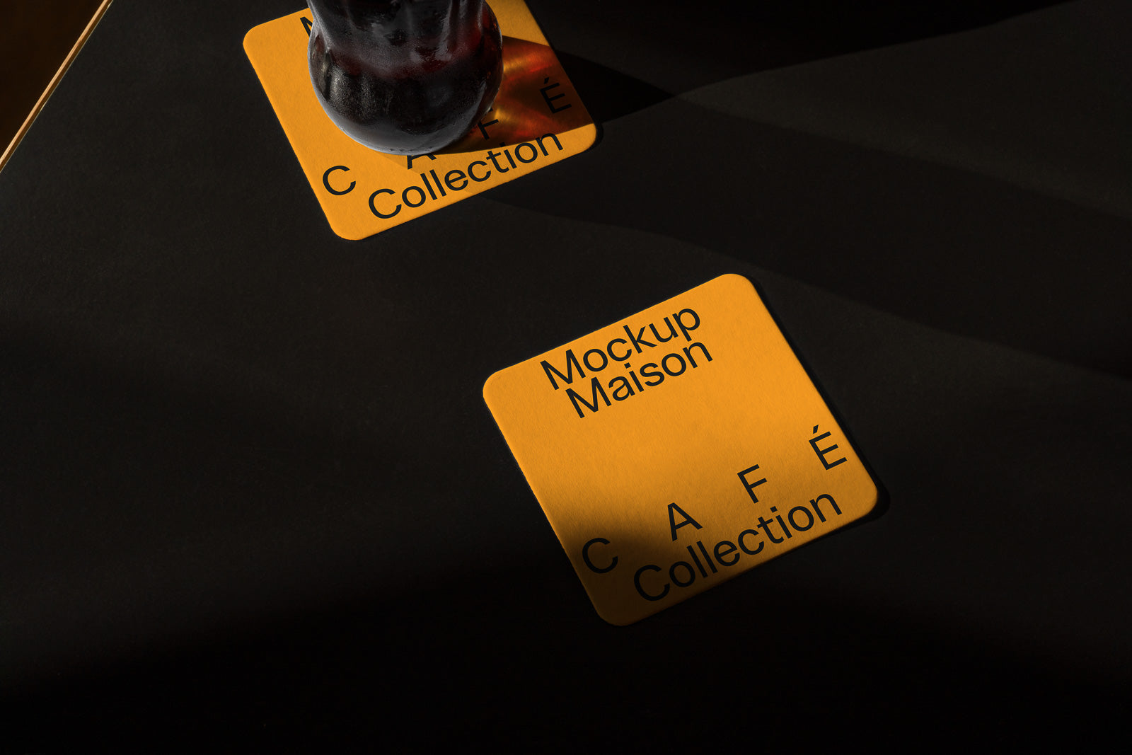PSD mockup of a yellow coaster with "Mockup Maison" and "CAFÉ Collection" text, placed on a dark surface with a glass resting on it.