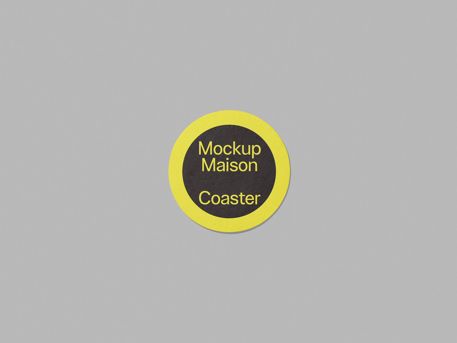 PSD mockup of a round coaster with a yellow outer ring and black center displaying the text "Mockup Maison Coaster" on a light gray background.