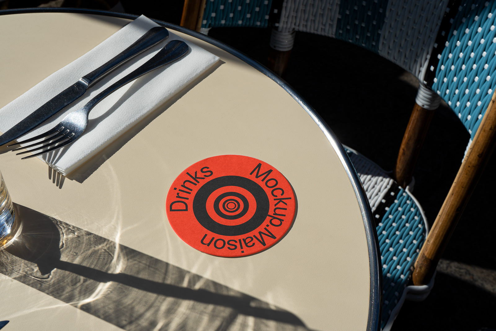PSD mockup of a round table setup with cutlery on a napkin and a red coaster labeled "Drinks" and "Mockup Maison," casting shadows.