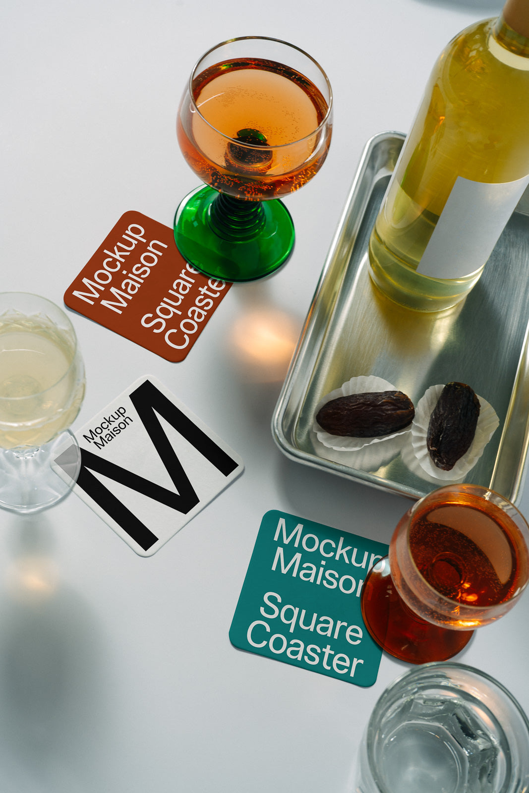 PSD mockup of square coaster under a glass containing a red liquid, with accompanying items like a wine bottle, dates, and drinkware on a metallic tray.