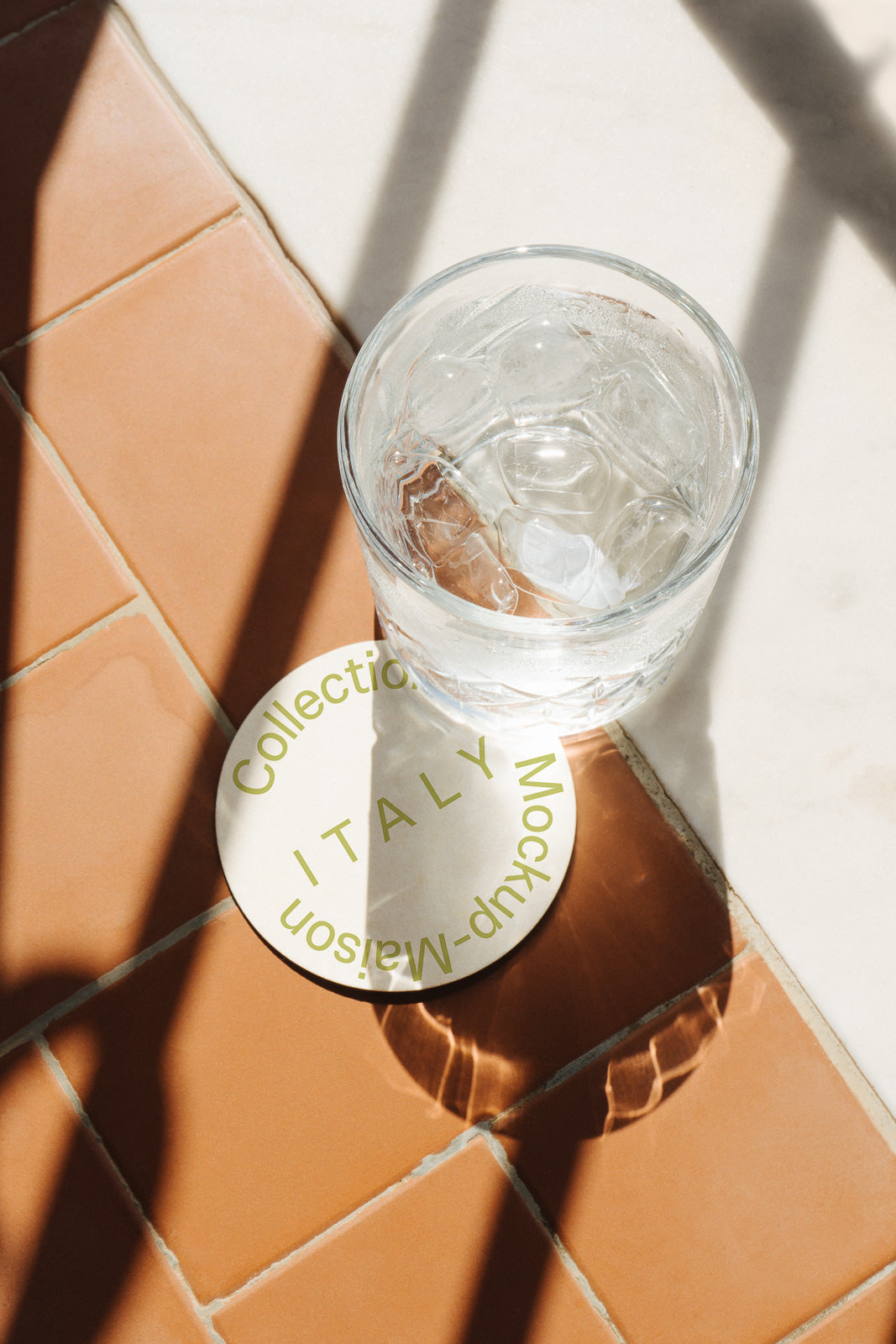 PSD mockup of a glass of water with ice on a coaster labeled "Collection Italy Maison Mockup." The background features terracotta tiles.