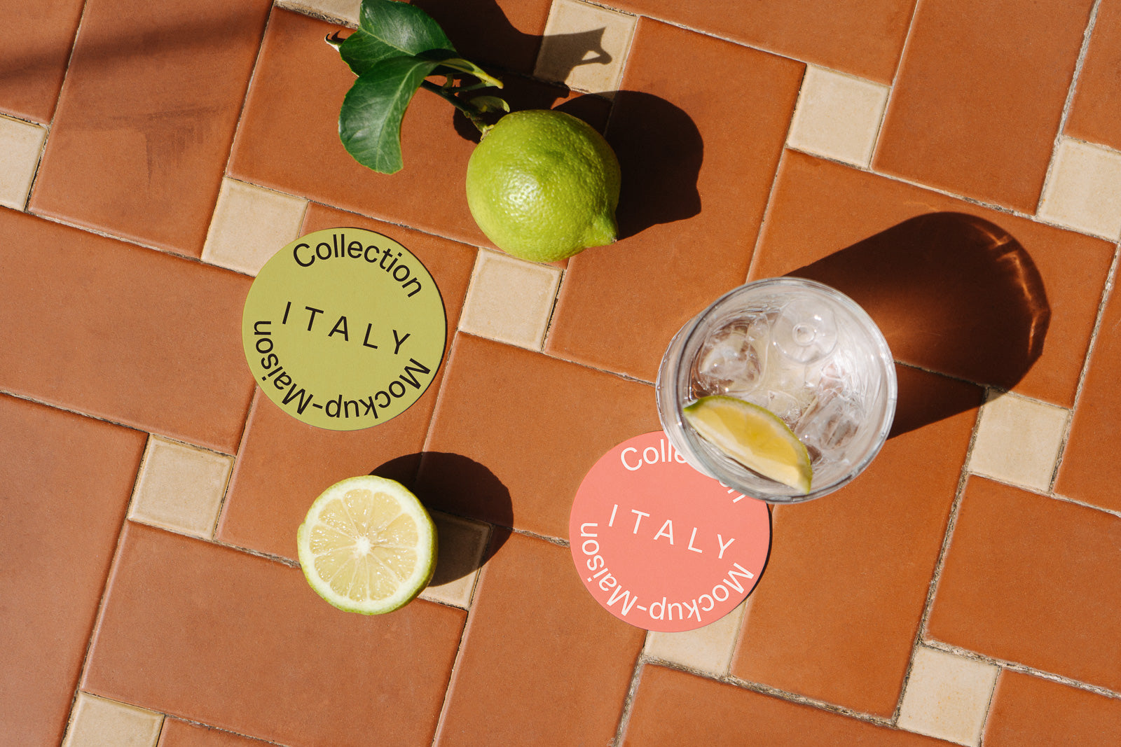 PSD mockup of a lemon and lime on terracotta tiles with two circular "Collection Italy" labels and a glass of iced water nearby.